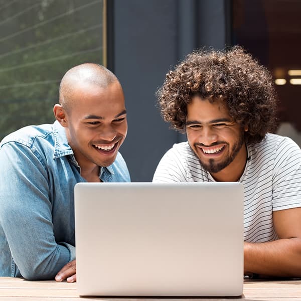 Two men smiling at a laptop screen outside