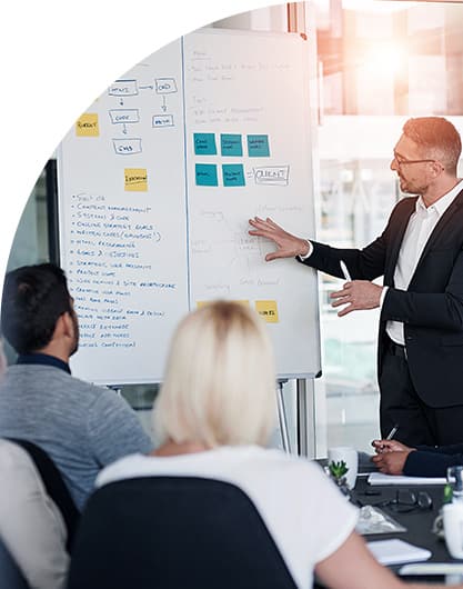 A person standing in front of a whiteboard full of post-it notes and diagrams, presenting to an audience.