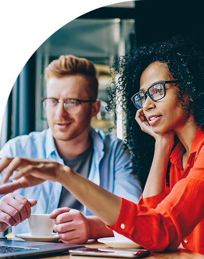 Two people with glasses, a man and a woman, are engaged in a discussion, pointing at a laptop screen. They appear focused and cooperative.