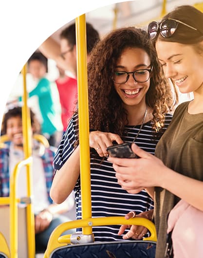 Two female friends having fun and looking at bus routes on their phone while waiting riding public transit
