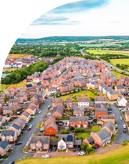 Aerial view of a modern suburban housing development with winding streets, red-brick homes, and surrounding green countryside.