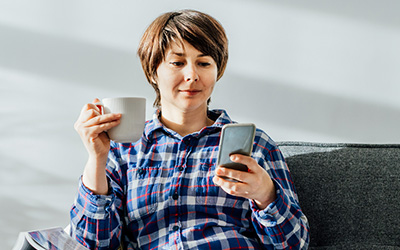 Woman looking at phone while drinking tea