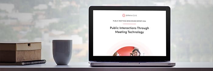 A laptop sits on a desk next to a mug, with the 2024 Public meetings benchmark report cover displayed on-screen.