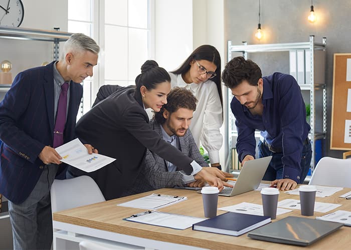 Colleagues in the office discuss a business project by comparing analysis data and graphs on a laptop