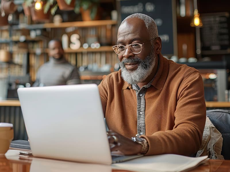 A black gentleman in his 60s sitting in a coffee shop while reading an email communication.