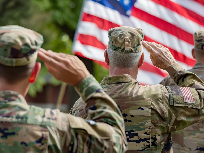 A group of veterans standing together and wearing military uniforms, with flags in the background.