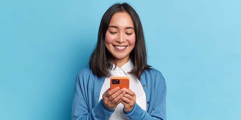 Asian American woman wearing blue communicating with her local government through Government Experience Agent (GXA) on her orange mobile phone.