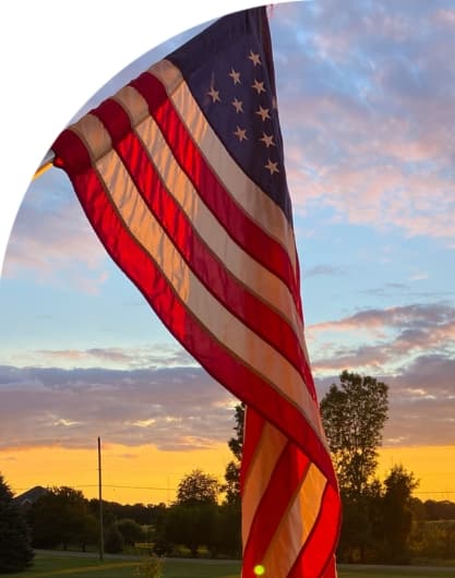 An American flag blows in the breeze as the sun sets in the background.