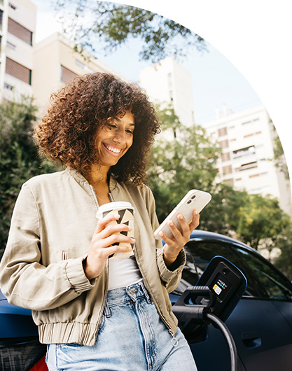 Person using mobile app while outdoors drinking a coffee and waiting by their car