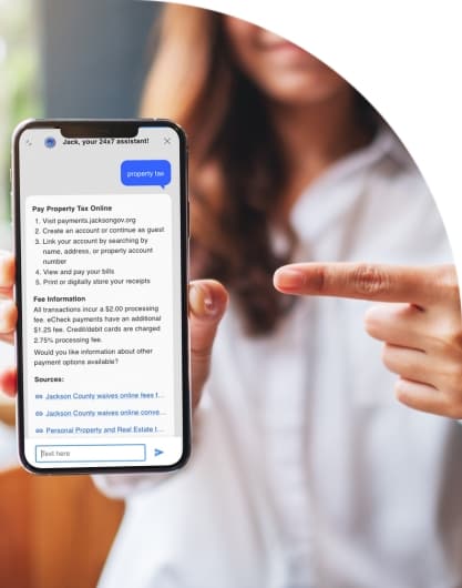 A woman holding a mobile phone and pointing to the screen, which is open to Granicus' Government Experience Agent (GXA).