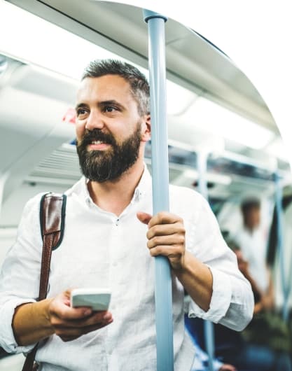 A person smiling and looking up from their phone while riding the tube.