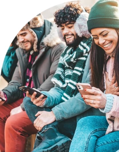 Students wearing winter hats smile as they scroll through their mobile phones.