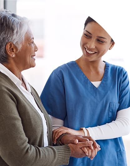 Caregiver supporting a senior woman, holding her hands indoors