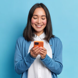 Asian American woman wearing blue communicating with her local government through Government Experience Agent (GXA) on her orange mobile phone