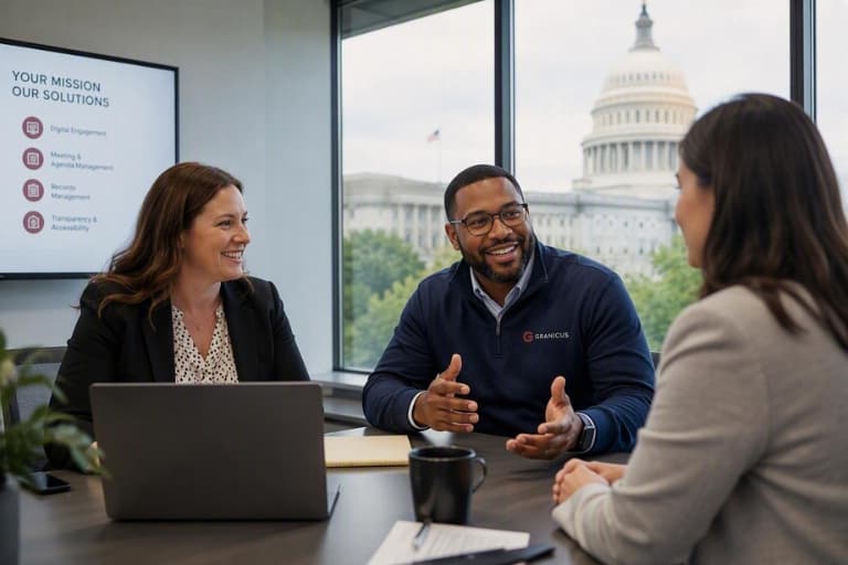 Three professionals seated around a conference table during a meeting, with a laptop, presentation screen, and the U.S. Capitol visible through large windows behind them.
