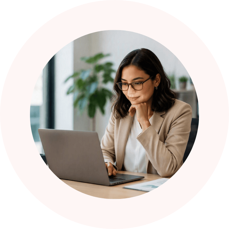 Person wearing glasses works on a laptop at a desk in a bright office, with blurred plants in the background.