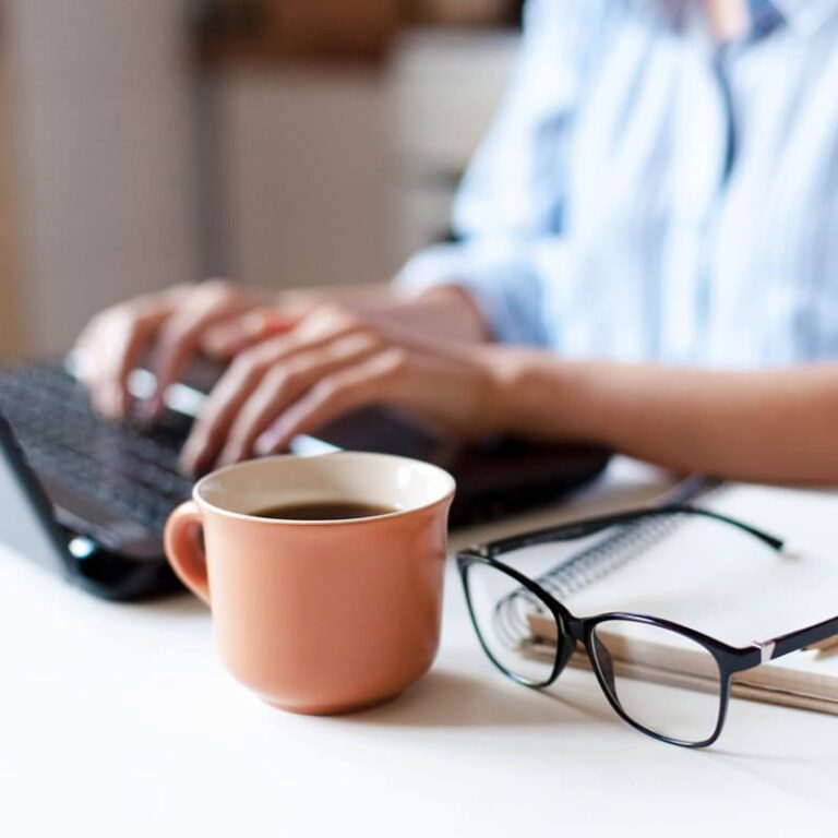 Close up of hands typing on a keyboard next to a cup of coffee