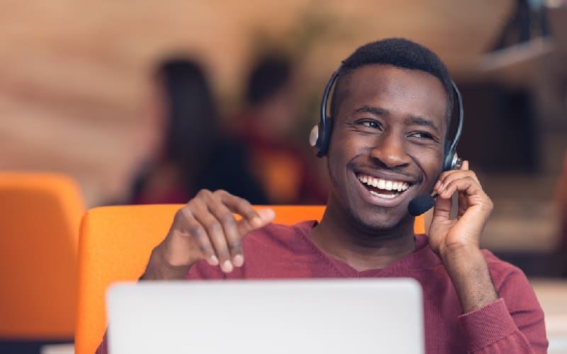 Smiling young adult black professional working remotely using his laptop and headset.