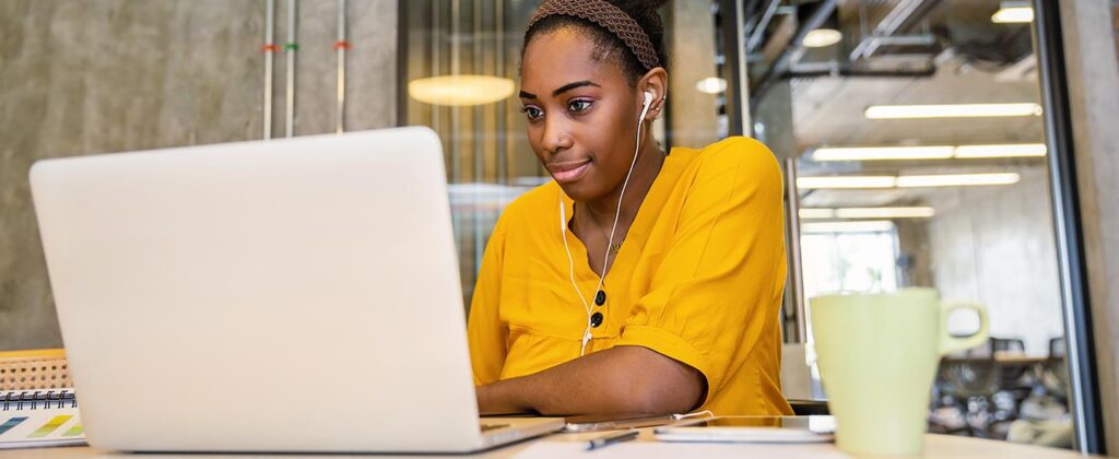 Young, professional black woman in a yellow shirt watching engaging content on her laptop.