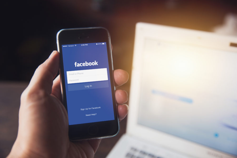 End of an Era – New Facebook Algorithm Marks Social Media’s Decline as Engagement Tool image Facebook App on iPhone with computer laptop background closeup male hand hold social network on smart device concept.