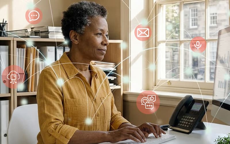 Person seated at a desk typing on a computer in an office, with icons representing email, chat, and notifications overlaid.