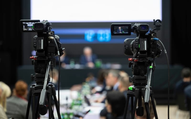 Video cameras recording a government meeting, highlighting the importance of captions for public broadcasts.