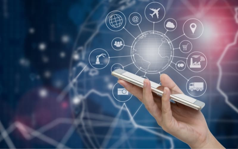 Hand holding a smartphone with digital icons and a globe, symbolizing digital transformation as an ongoing mindset.