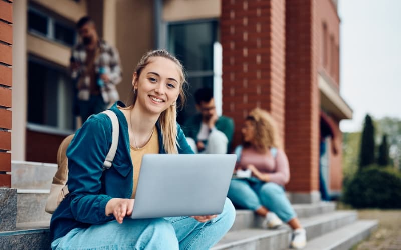 Students on campus steps using laptops and devices, representing the connection between online engagement and in-person learning.