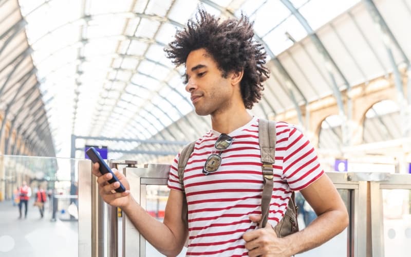 A person checks a smartphone while standing in a bright, modern transit station, reflecting how accessible digital services support ease, satisfaction, and everyday happiness in modern government experiences.