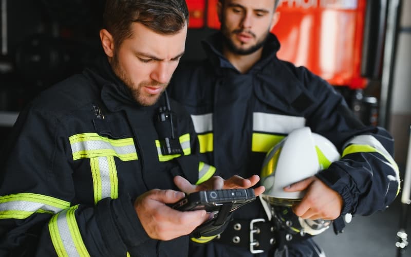 Firefighters using a handheld device near firefighting equipment, illustrating data-driven emergency response.