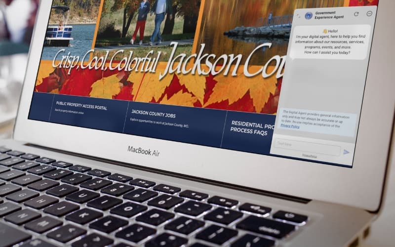 Laptop displaying the Jackson County website alongside the Granicus Government Experience Agent chat window, illustrating AI-driven support for public services.