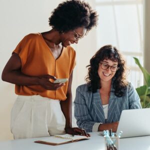 Two people working together at a desk, one using a laptop and the other holding a smartphone.