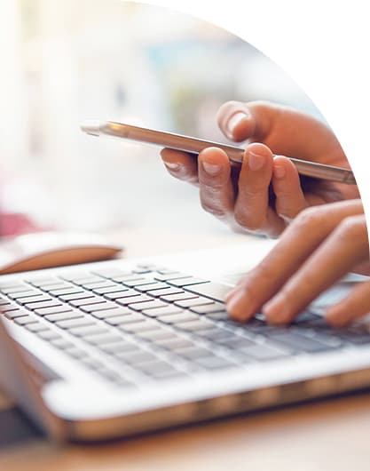 Close-up of hands using a smartphone while typing on a laptop keyboard, with a blurred background.