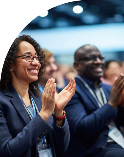 Smiling individuals in a crowd clapping, wearing business attire. The atmosphere is positive and engaged, suggesting a professional event or conference.