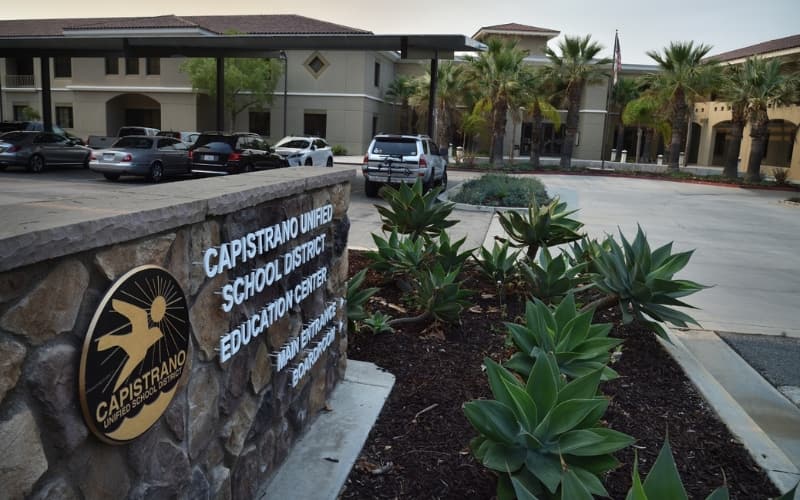 Entrance sign for Capistrano Unified School District Education Center with the building and parking lot in the background.