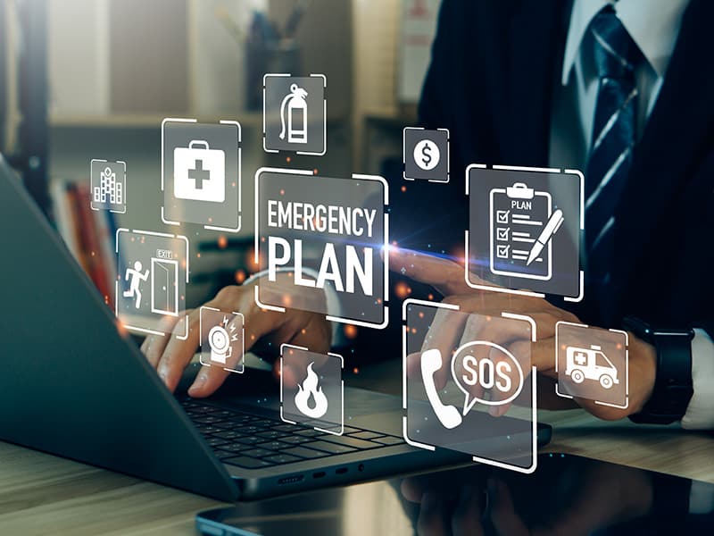 A government employee using a laptop, with overlay icons representing disaster preparedness tools, including emergency plan, SOS, and phone symbols.