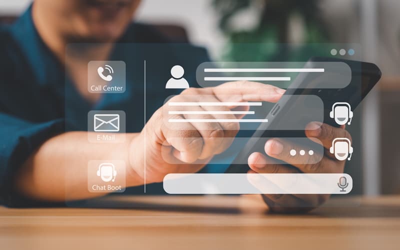 Person using a smartphone with virtual icons for call center, email, and chatbot displayed on the screen.