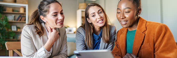 Three female government colleagues reviewing civic participation results using Operations Cloud on a laptop.