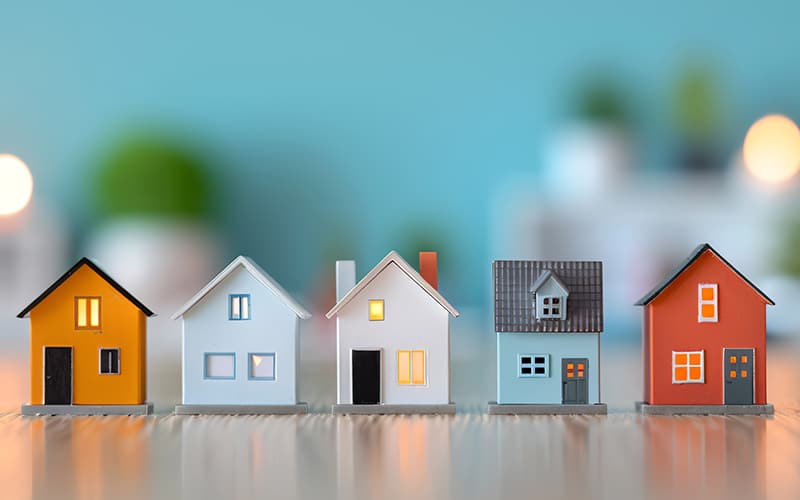 A row of colorful models of short-term rental homes made from paper against a teal blue background.