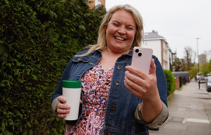 Middle aged blonde woman walking down the street with coffee while reading a SMS text response from her local government.