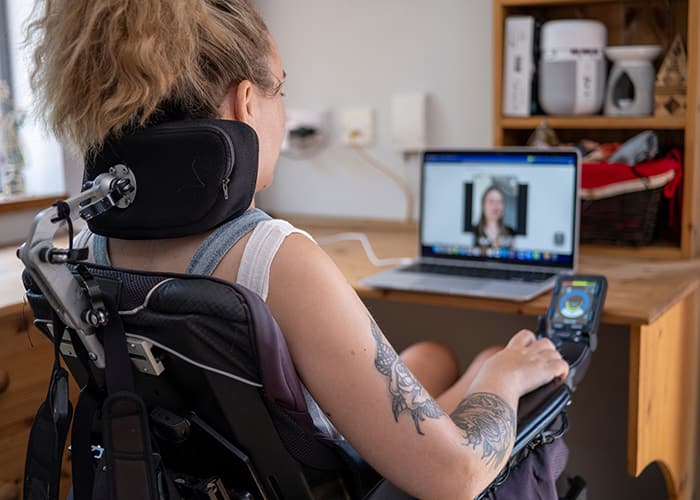 Woman in electric wheelchair using built in accessibility features to understand a streamed public meeting.